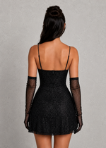 Woman wearing a black dress with thin straps and sheer gloves on a gray background