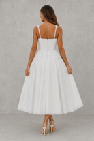 Woman wearing a white dress with thin straps against a gray background
