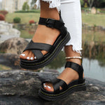 Black sandals worn by a person sitting on a rock with a blurred natural background