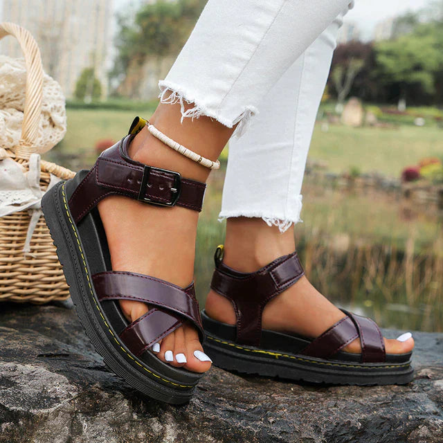Brown sandals worn with white jeans on a stone surface with a natural background