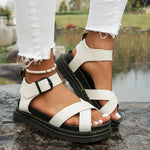 White sandals with black soles worn by a person standing on a stone surface.