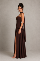 Woman wearing a brown strapless gown with a slit on a plain background