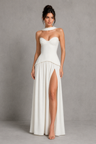 Woman wearing a white strapless gown with a high slit on a gray background