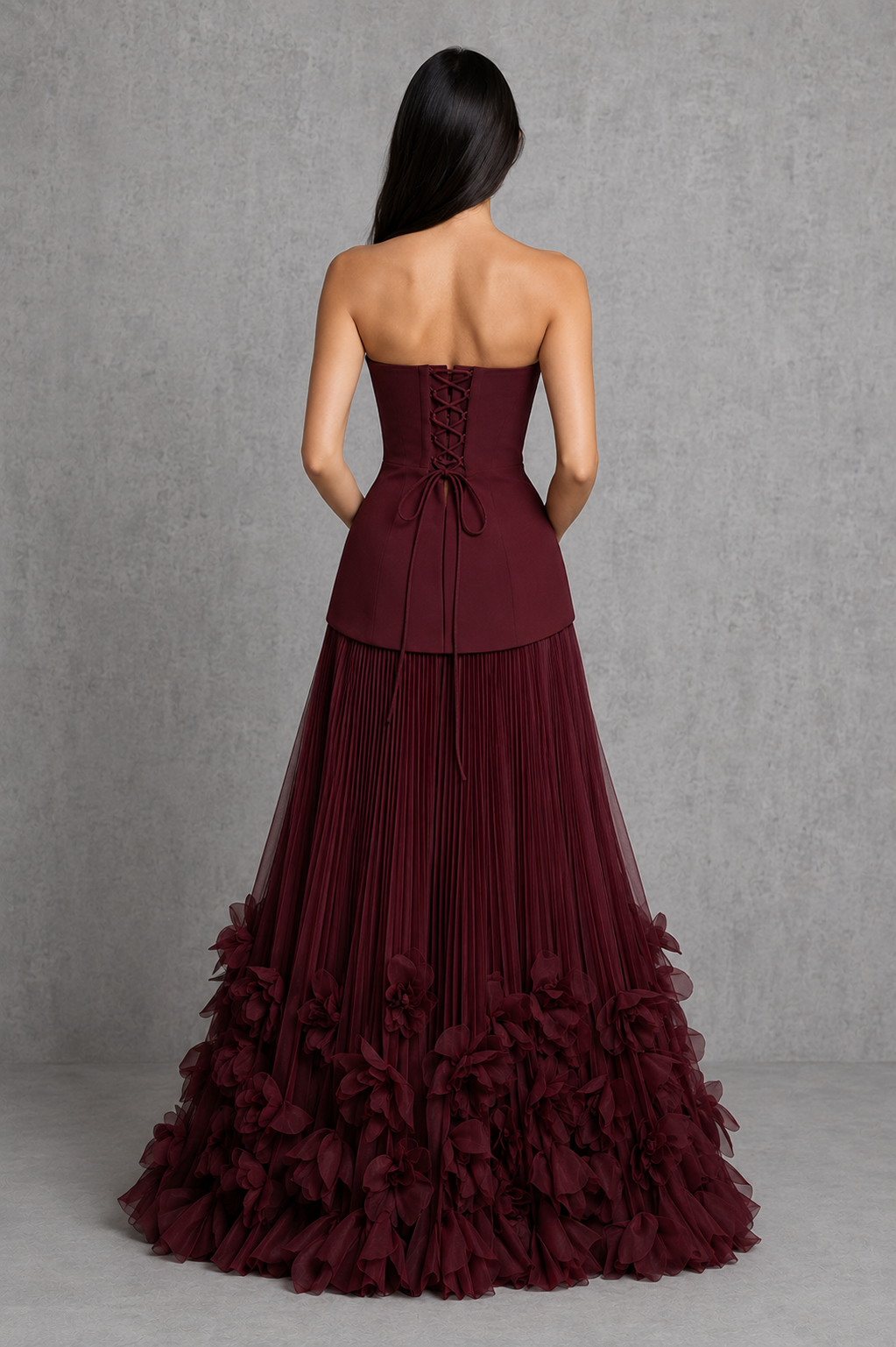 Women’s cherry lacquer strapless corset gown with a lace-up back, pleated full skirt, and handcrafted floral appliqué hem