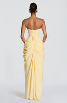 Woman wearing a strapless yellow evening gown on a plain background