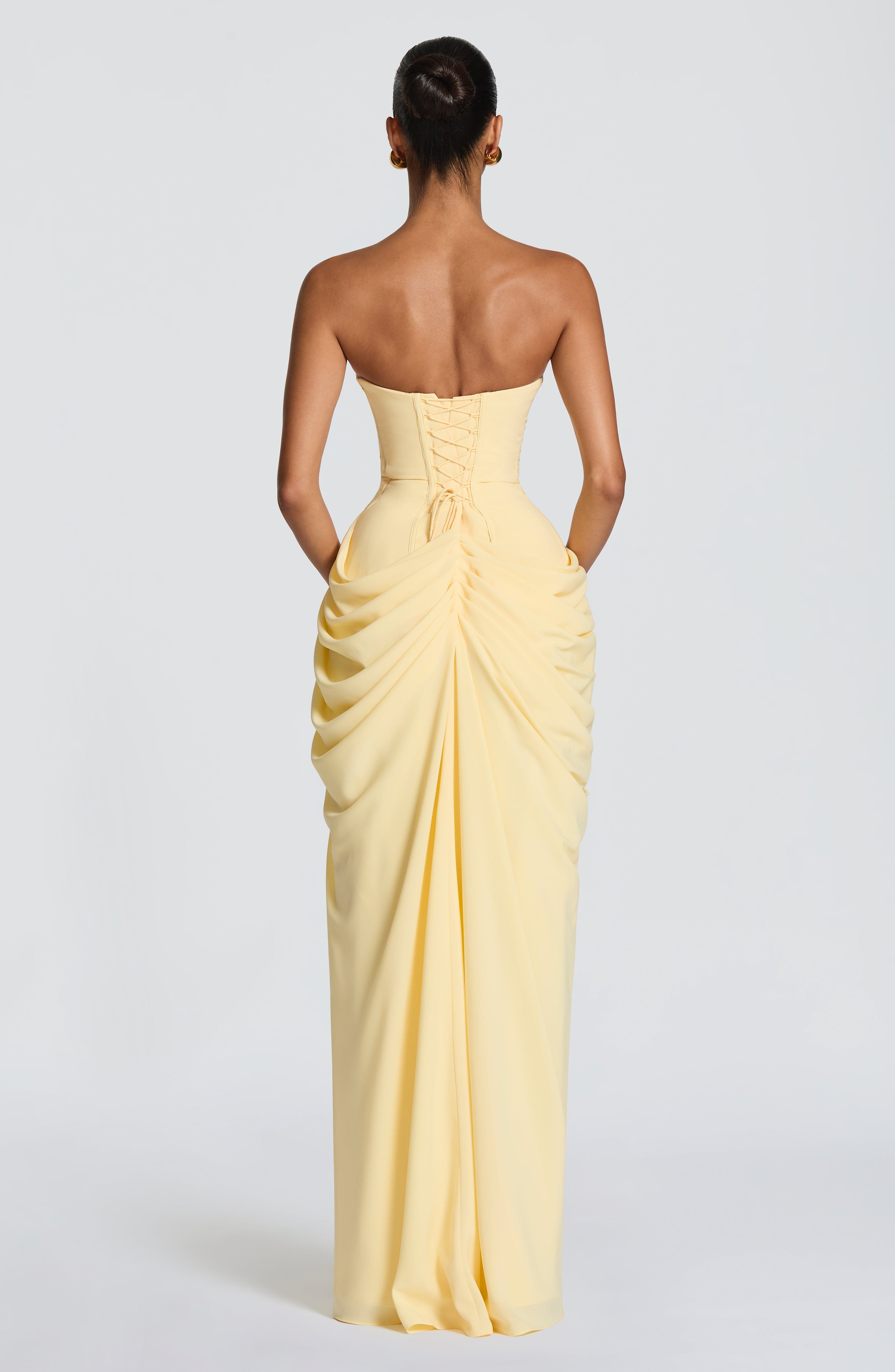 Woman wearing a strapless yellow evening gown on a plain background
