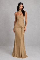 Woman wearing a beige strapless gown against a plain background