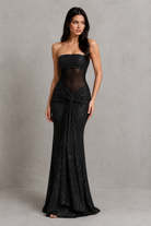 Woman wearing a black strapless gown with sheer overlay against a gray background