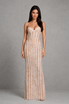 Woman wearing a strapless, long, beige lace dress against a gray background