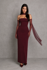 Woman wearing a burgundy evening gown with sheer sleeves against a gray background