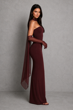 Woman wearing a burgundy one-shoulder gown with a cape against a gray background