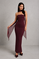 Woman wearing a burgundy strapless gown with a sheer overlay against a gray background
