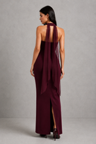 Woman wearing a burgundy halter neck dress with sheer overlay on a gray background