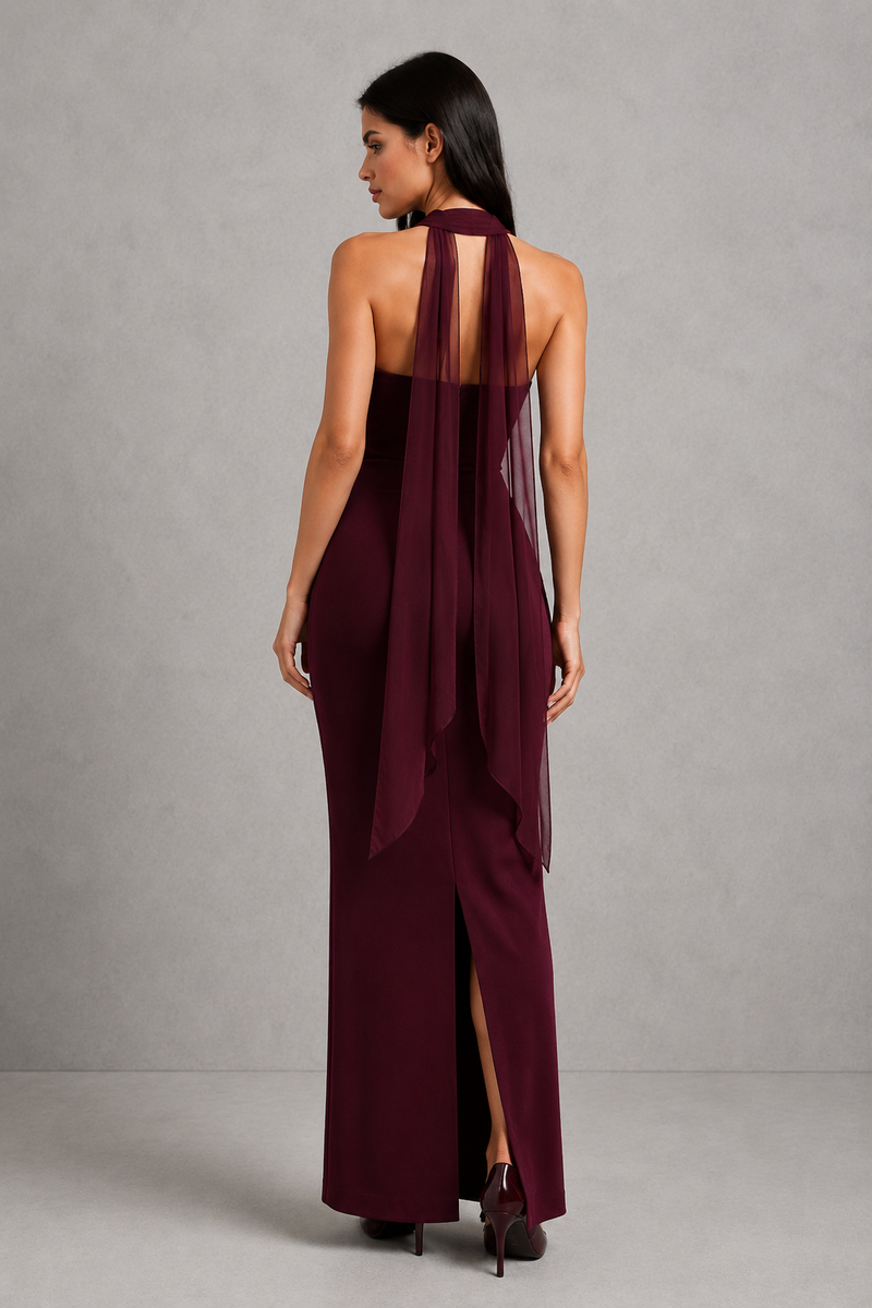 Woman wearing a burgundy halter neck dress with sheer overlay on a gray background