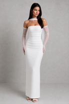 Woman wearing a white off-shoulder dress with sheer sleeves against a gray background