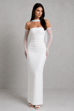 Woman wearing a white off-shoulder dress with sheer sleeves against a gray background
