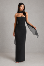 Woman wearing a black strapless gown with a sheer overlay against a gray background