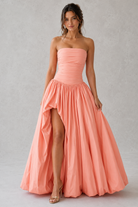 Woman wearing a strapless pink gown with a high slit on a plain background