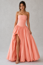 Woman wearing a strapless pink gown with a high slit on a plain background