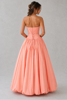 Woman wearing a strapless coral gown against a plain background