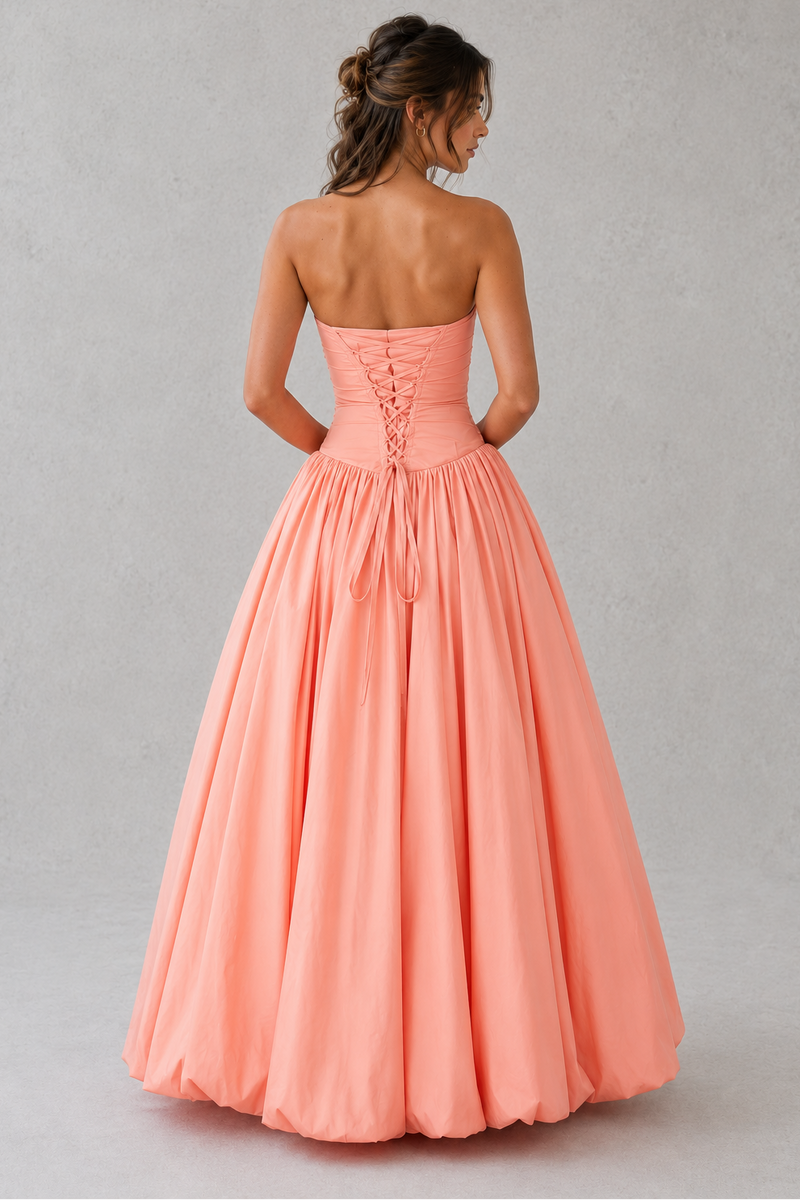 Woman wearing a strapless coral gown against a plain background