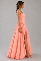 Woman wearing a coral pink strapless gown with a slit on a gray background