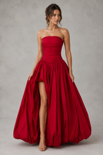 Woman wearing a strapless red gown with a slit on a plain background