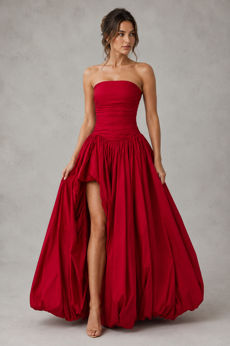 Woman wearing a strapless red gown with a slit on a plain background