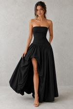 Woman wearing a black strapless gown with a high slit on a gray background
