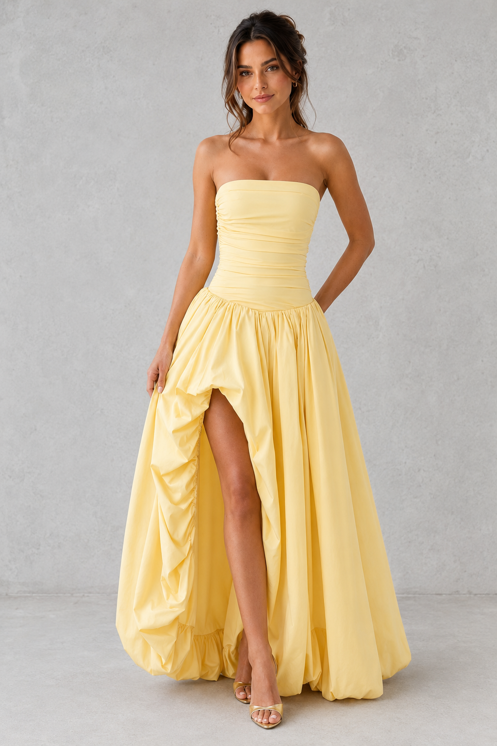 Woman wearing a yellow strapless gown with a high slit on a gray background
