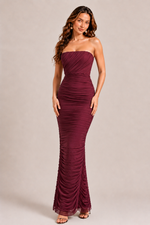 Woman wearing a burgundy strapless gown on a beige background