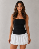 Woman wearing a black strapless top and white skirt against a gray background