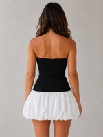 Woman wearing a black strapless top and white skirt against a gray background