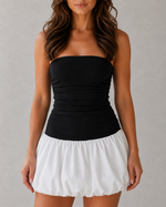 Woman wearing a black strapless top and white skirt against a gray background