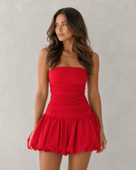Woman wearing a red strapless dress against a plain background