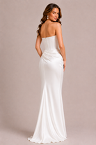 Woman wearing a strapless white evening gown against a beige background