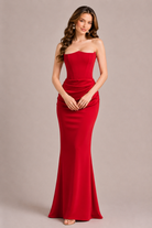 Woman wearing a strapless red evening gown against a plain background