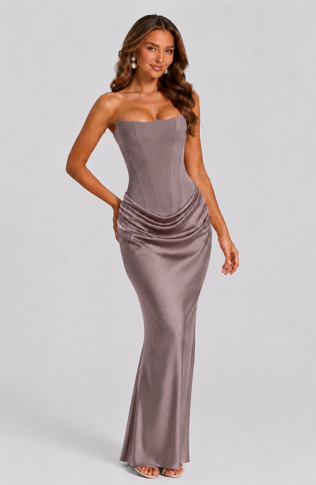 Woman wearing a strapless, floor-length dress on a plain background