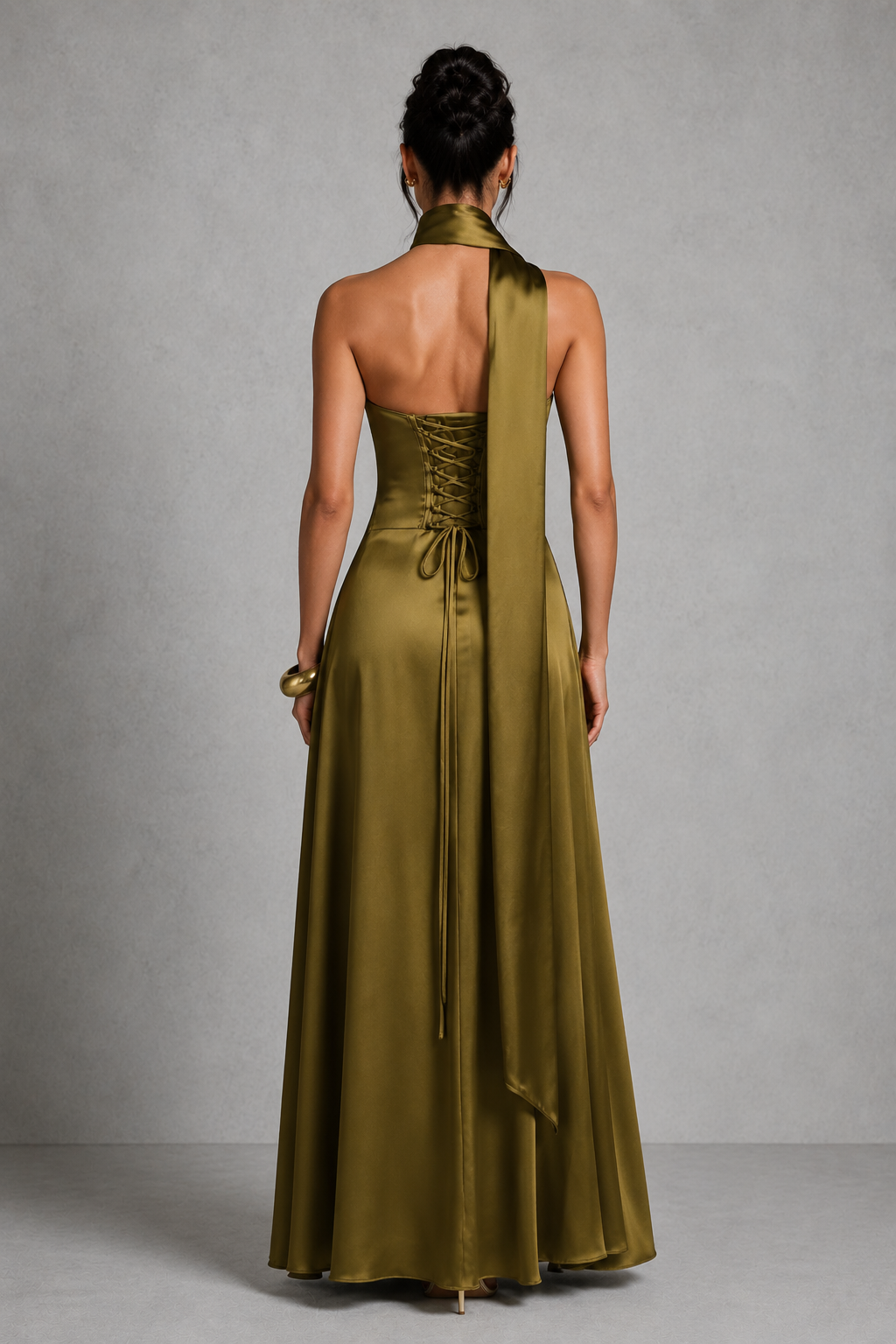 Woman wearing a long green dress with a halter neck design against a gray background