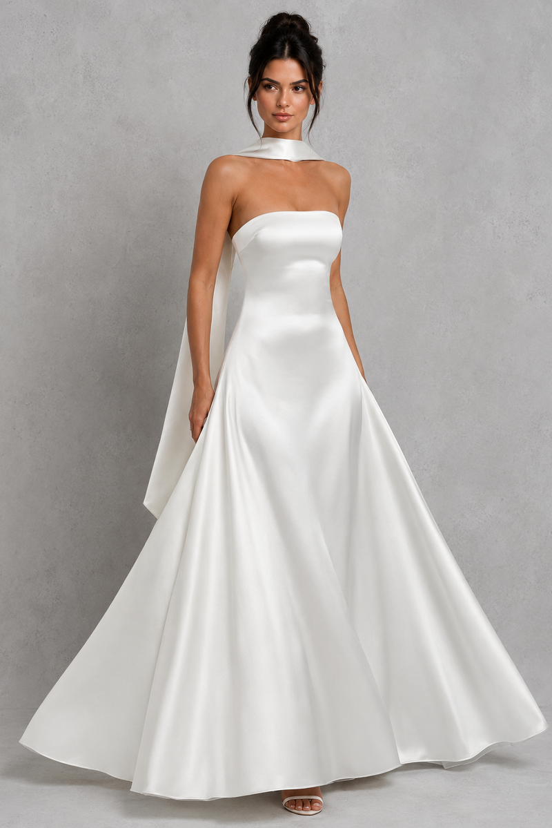Woman wearing a strapless white wedding dress with a cape on a gray background