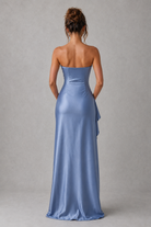 Woman wearing a strapless blue evening gown against a gray background