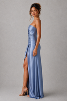 Woman wearing a blue strapless gown with a slit on a gray background