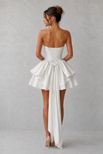 Woman wearing a strapless white dress with ruffled skirt on a plain background