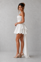 Woman wearing a strapless white dress with a long train against a gray background