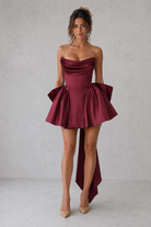 Woman wearing a burgundy strapless dress with a ruffled skirt on a plain background