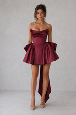 Woman wearing a burgundy strapless dress with a ruffled skirt on a plain background