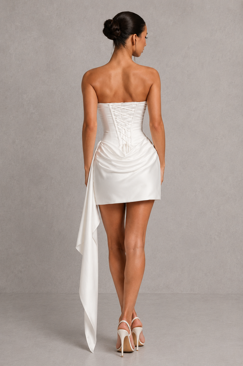 Woman wearing a strapless white dress with a draped effect on a gray background