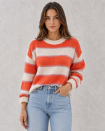 Woman wearing a red and white striped sweater with blue jeans against a gray background