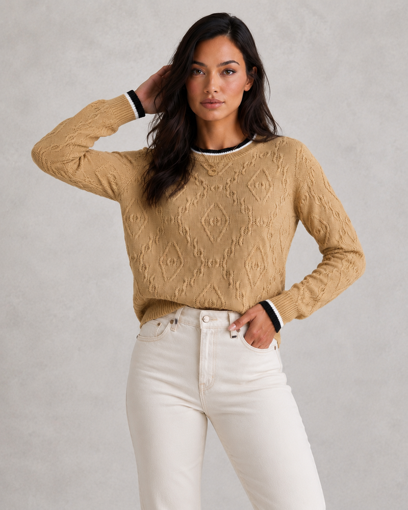 Woman wearing a beige cable knit sweater and white pants against a gray background
