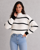 Woman wearing a white sweater with black stripes and blue jeans against a gray background
